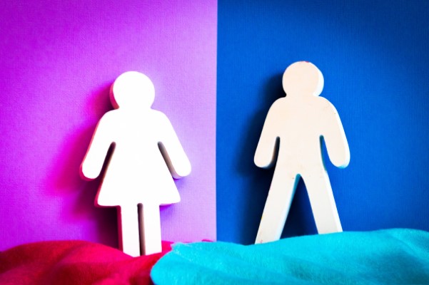 Zwei Figuren, eine weiblich, die andere männlich stehen vor einer farblich geteilten Wand.