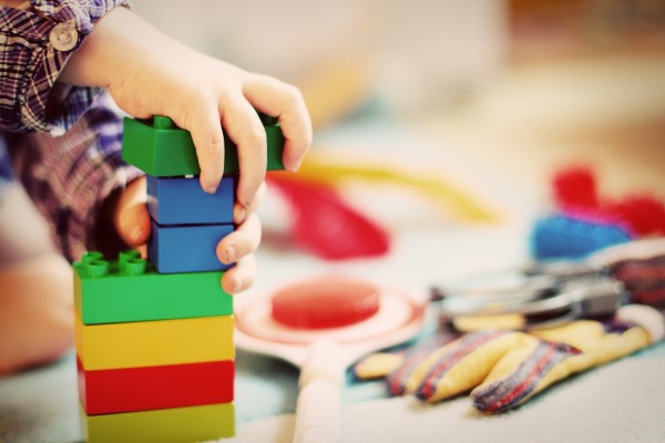 Ein kleines Kind spielt mit Duplo-Steinen und baut daraus einen Turm.