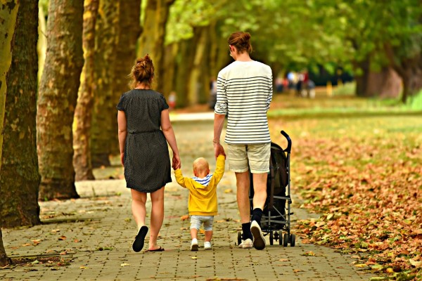 Eine junge Mutter und ein junger Vater mit einem Kleinkind laufen eine Allee entlang
