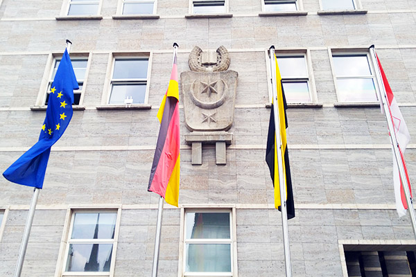 Ausschnitt der Fassade des Rathauses in Halle (Saale) mit dem Stadtwappen, davor stehen 4 Flaggen, die europäische, die deutsche, die des Landes Sachsen-Anhalt sowie die hallesche Flagge.