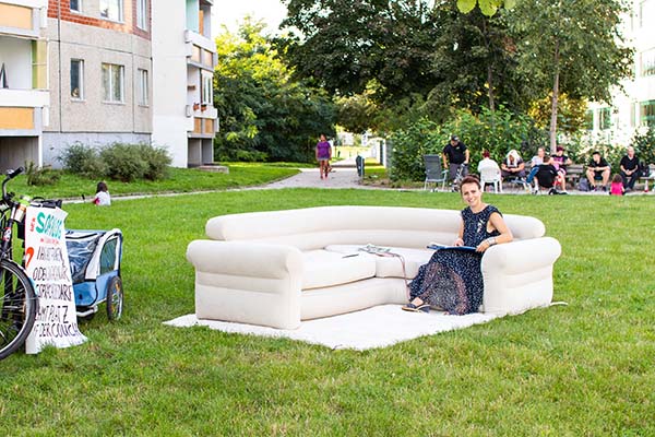 Stadträtin Dörte Jacobi auf einem aufblasbaren Sofa in Heid-Nord, daneben ihr Fahrrad. Im Hintergrund sitzen Leute. Links befindet sich ein Wohnblock.