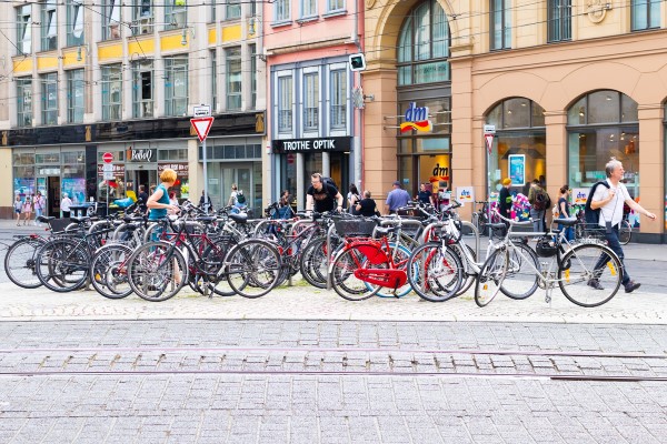 Verkehrsinsel zwischen Straßenbahnschienen mit vielen Fahrradbügeln und angeschlossenen Fahrrädern sowie vereinzelt umherlaufenden Menschen