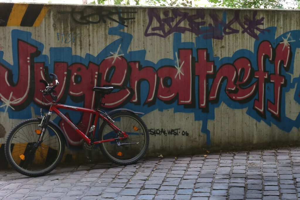 Eine Holzwand mit dem roten Graffiti-Schriftzug "Jugendtreff" an der links vorn ein rotes Fahrrad lehnt